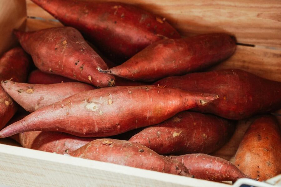 Close-up of fresh sweet potatoes in a wooden crate, ideal for cooking.