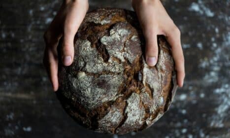 Close-up of hands holding a rustic loaf of whole wheat bread with a dark, textured crust.