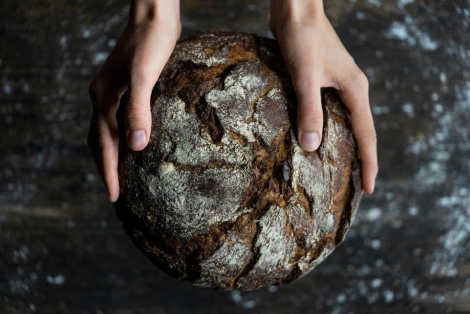 Close-up of hands holding a rustic loaf of whole wheat bread with a dark, textured crust.