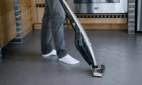 A person cleaning a tiled floor with a modern vacuum cleaner indoors.