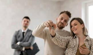 A joyful couple holding keys to their new home with a realtor in the background.