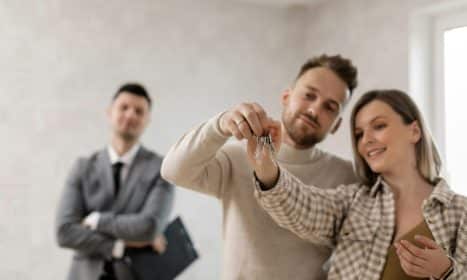 A joyful couple holding keys to their new home with a realtor in the background.