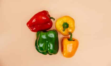 A vibrant display of red, green, yellow, and orange bell peppers arranged on a simple background.
