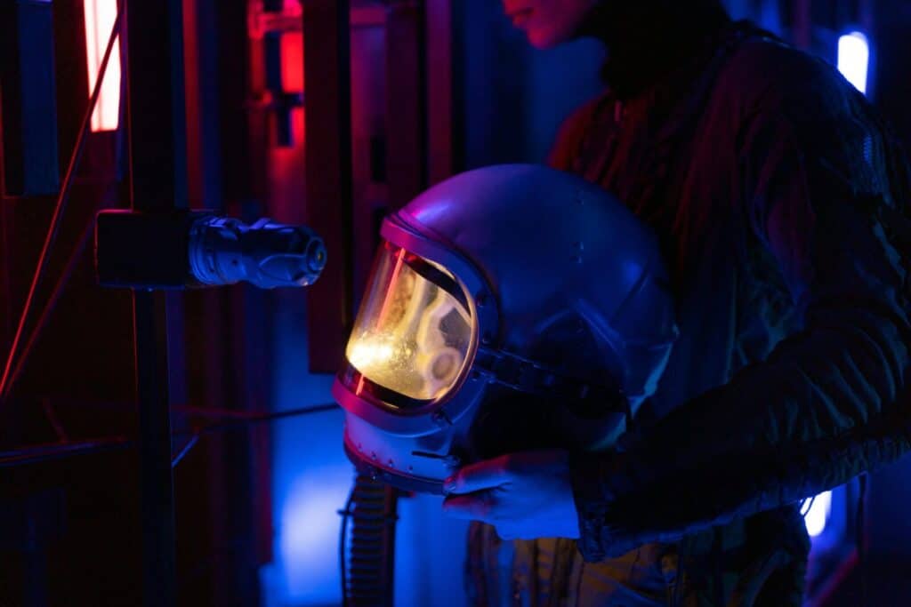 Astronaut holding helmet in blue and red lit futuristic setting.