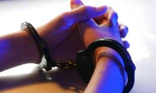Close-up of handcuffed hands under blue police light, signifying arrest or detention.