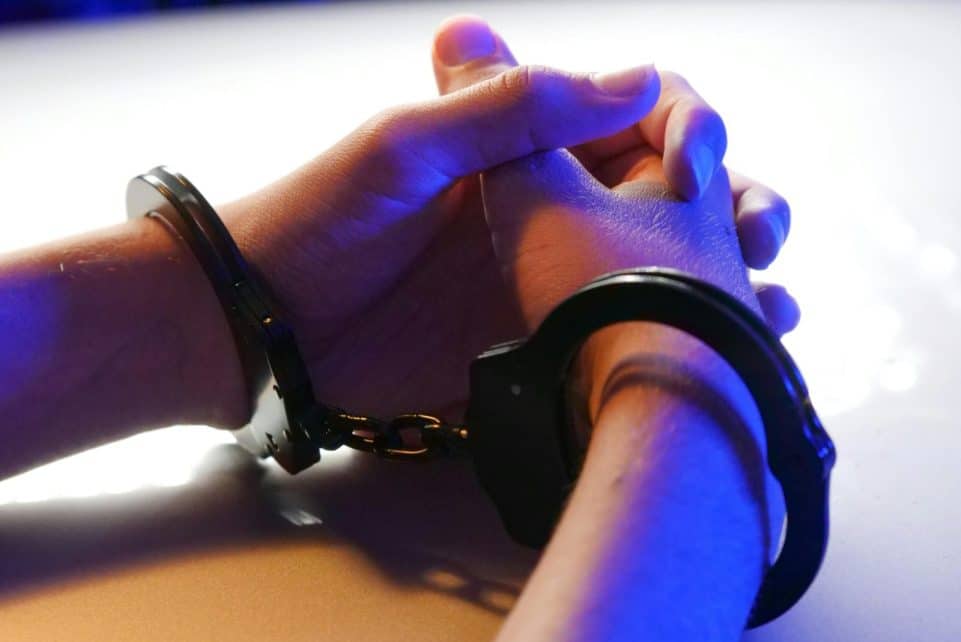 Close-up of handcuffed hands under blue police light, signifying arrest or detention.