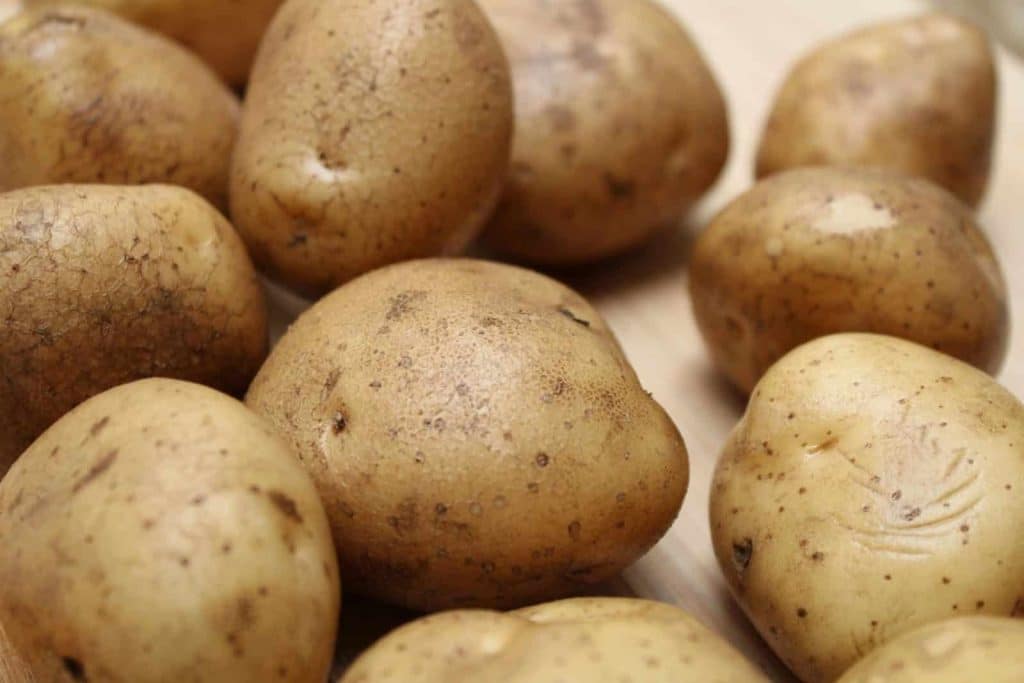 High-quality close-up photo of fresh raw potatoes on a wooden surface, ideal for food and culinary themes.