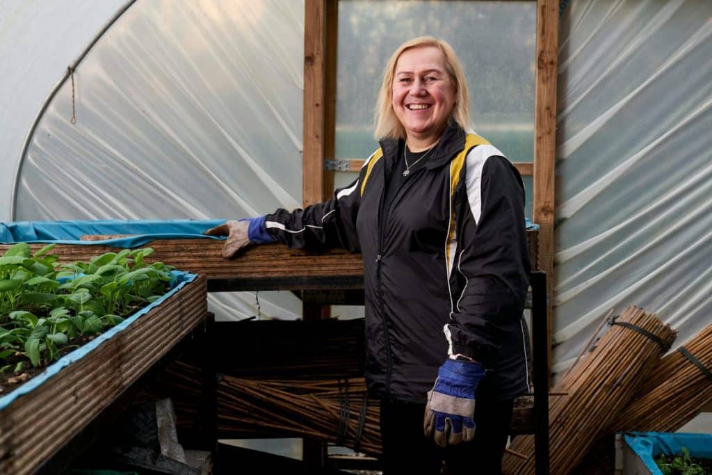 An elderly woman enjoying gardening in a greenhouse in Greater Manchester.
