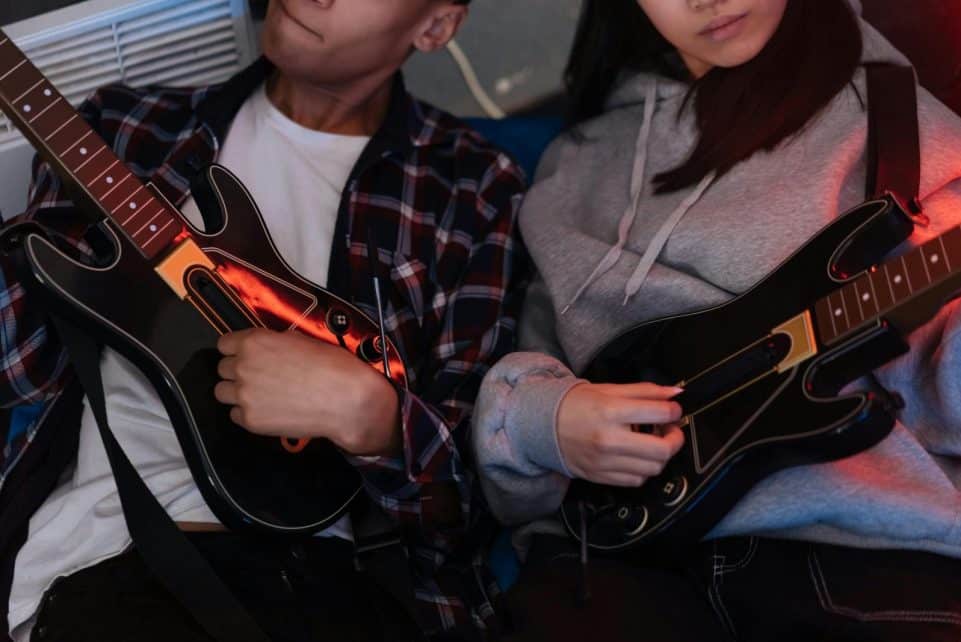 Two friends enjoying Guitar Hero game session, focusing on teamwork and fun.