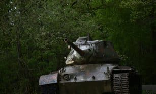 Old rusty battle tank parked in dense green forest, highlighting history and nature contrast.
