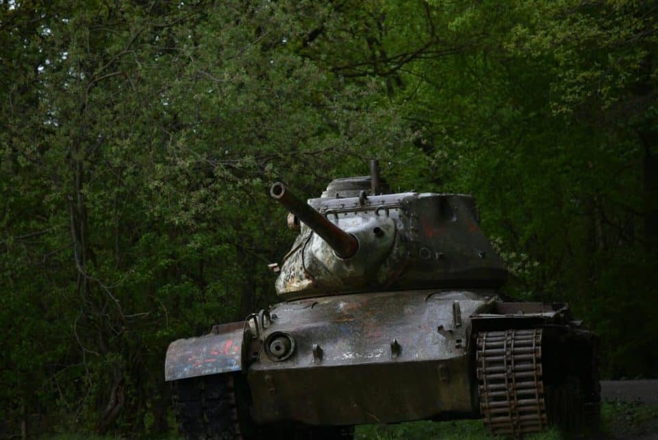 Old rusty battle tank parked in dense green forest, highlighting history and nature contrast.