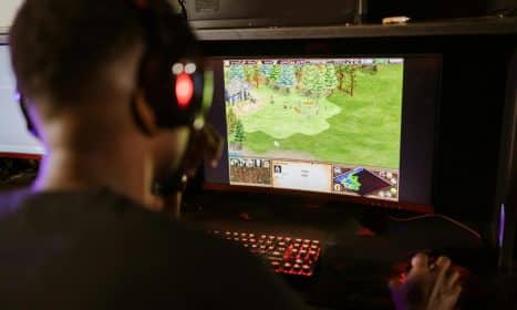 A gamer intensely playing a strategy game on a high-resolution monitor indoors.