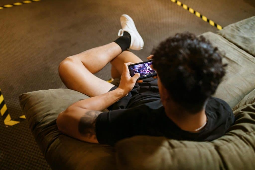A man relaxing on a sofa playing a video game on his smartphone.