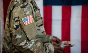 Close-up of a soldier in military uniform with American flag patch and background.