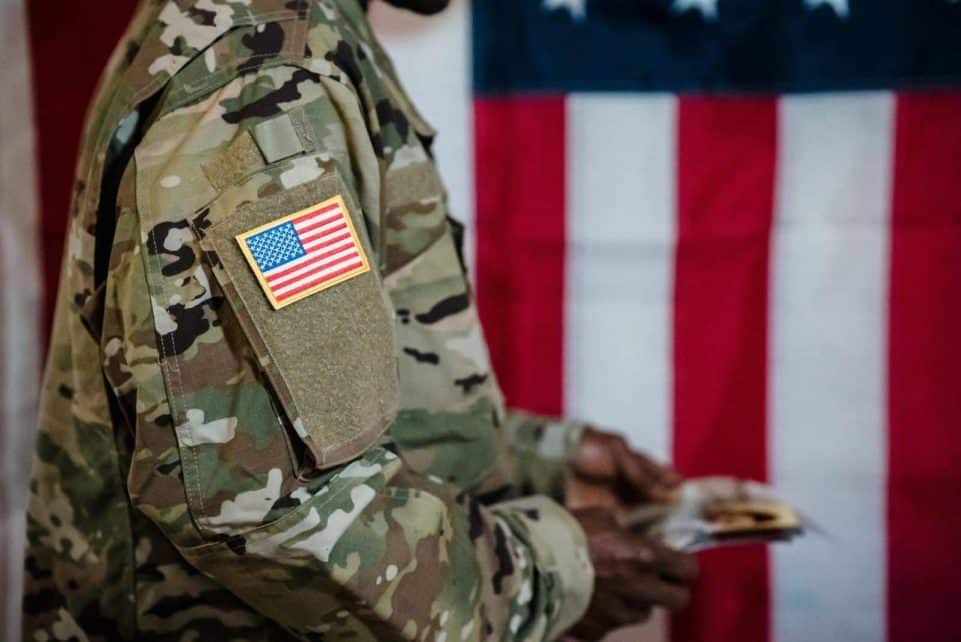 Close-up of a soldier in military uniform with American flag patch and background.