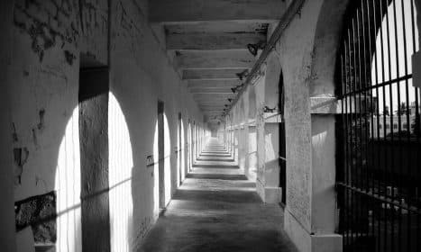 Black and white image of a historic jail corridor in India with iron bars and cement pillars.