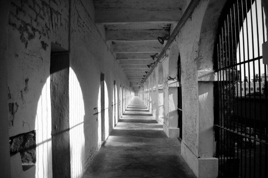 Black and white image of a historic jail corridor in India with iron bars and cement pillars.