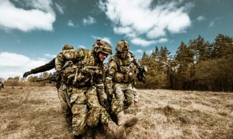 Military personnel actively engaged in outdoor rescue operation on grassy field, showcasing teamwork and bravery.