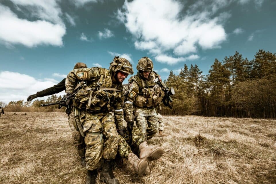 Military personnel actively engaged in outdoor rescue operation on grassy field, showcasing teamwork and bravery.