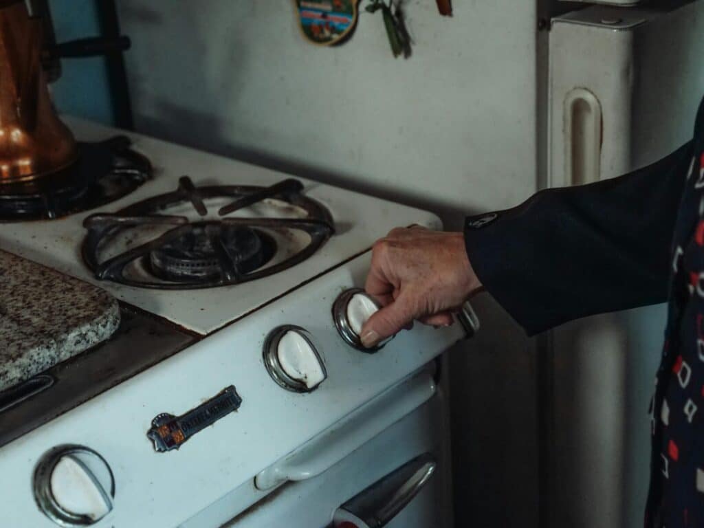 Close-up of a hand turning a knob on a retro gas stove in a home kitchen setting.