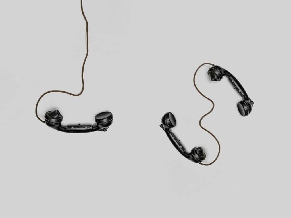 Two vintage black telephone handsets connected by cords on gray background.