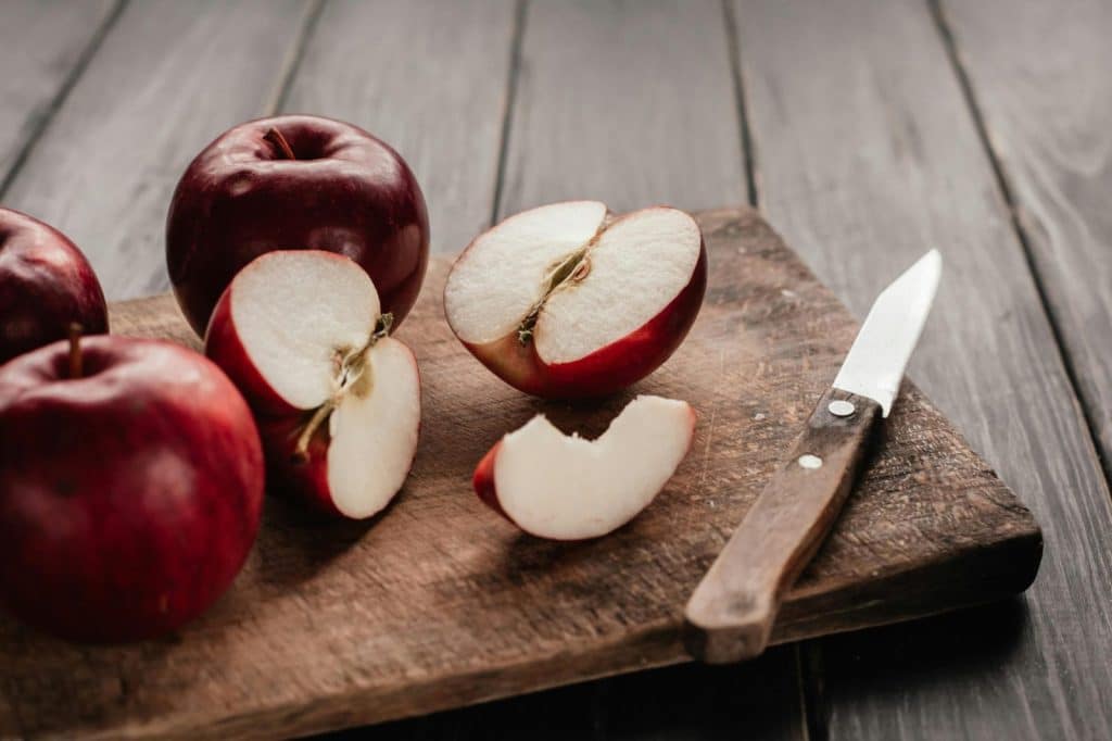 Top view of fresh red apples sliced on a rustic wooden chopping board with a knife.