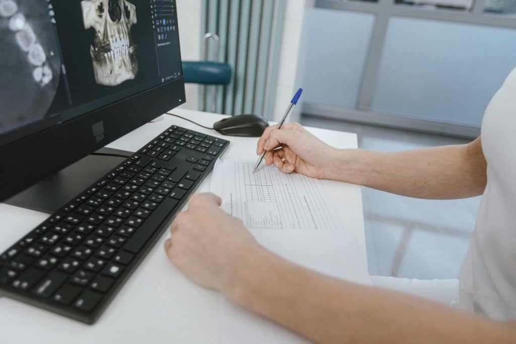 Close-up of a healthcare worker analyzing x-ray results and taking notes on a computer desk.