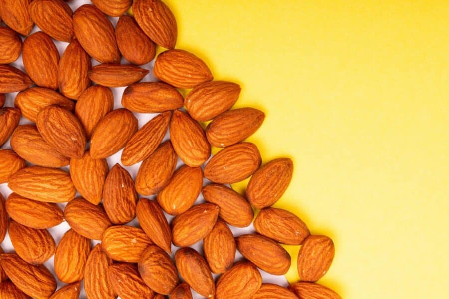A flatlay of almonds on a vibrant yellow backdrop with ample copy space.