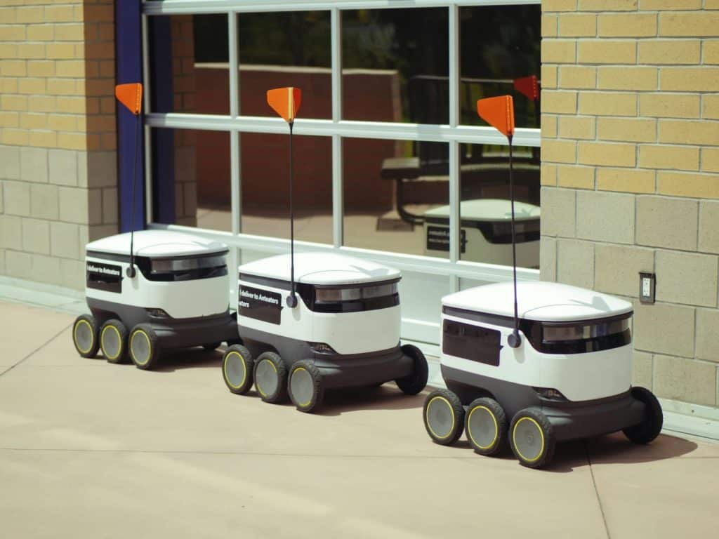 Three autonomous delivery robots parked outside a building, showcasing modern technology.