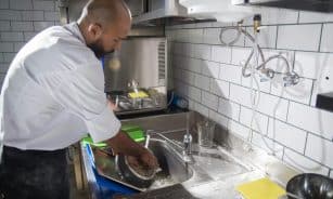 A chef cleans kitchen utensils in a stainless steel sink, maintaining hygiene standards.