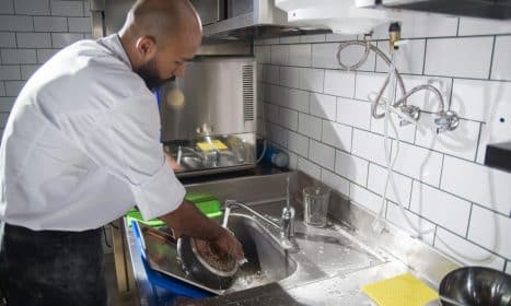 A chef cleans kitchen utensils in a stainless steel sink, maintaining hygiene standards.