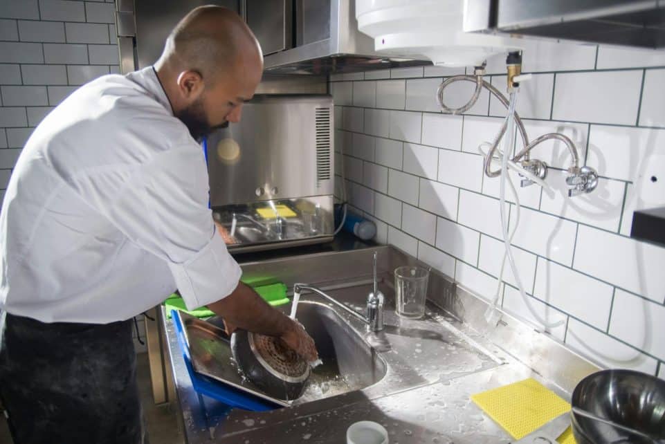 A chef cleans kitchen utensils in a stainless steel sink, maintaining hygiene standards.