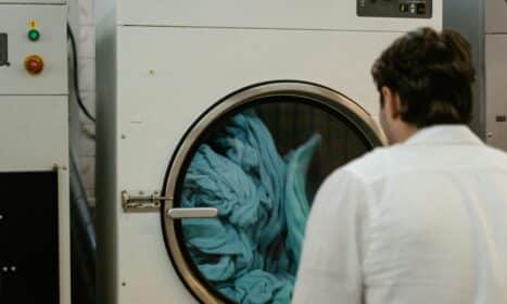 A man watches a washing machine spin in a laundromat, focusing on the process.
