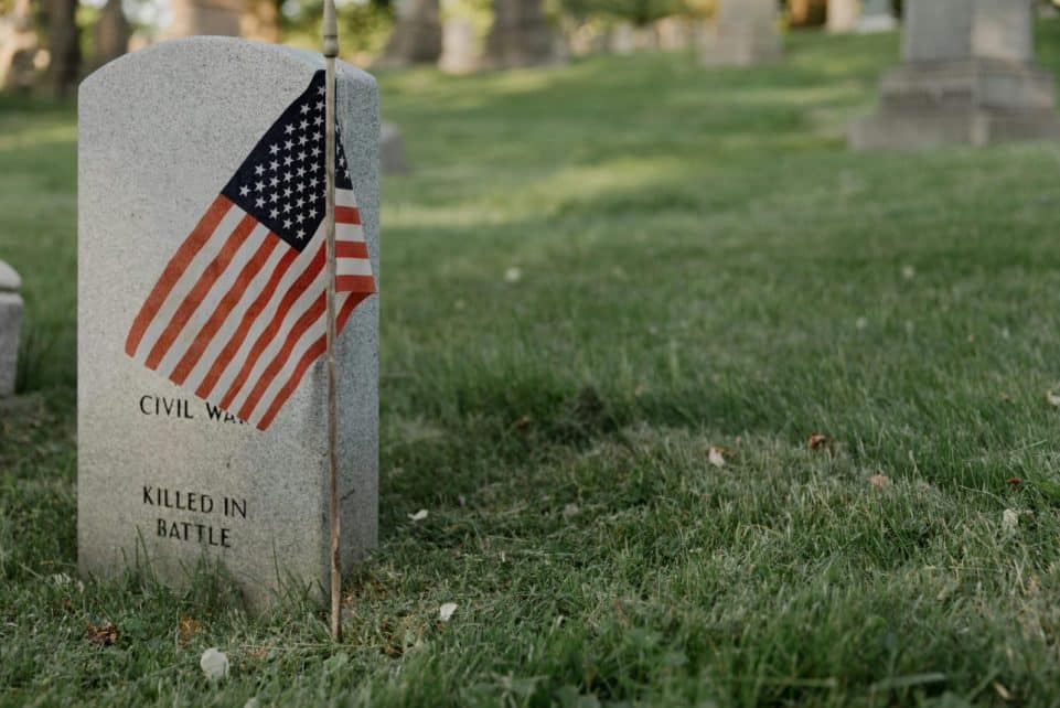 A gravestone with an American flag in a cemetery, honoring a civil war veteran.