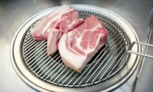 Close-up of raw pork slices on a Korean BBQ grill, ready for cooking.