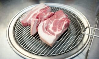 Close-up of raw pork slices on a Korean BBQ grill, ready for cooking.