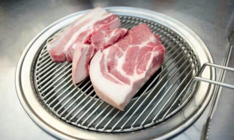 Close-up of raw pork slices on a Korean BBQ grill, ready for cooking.