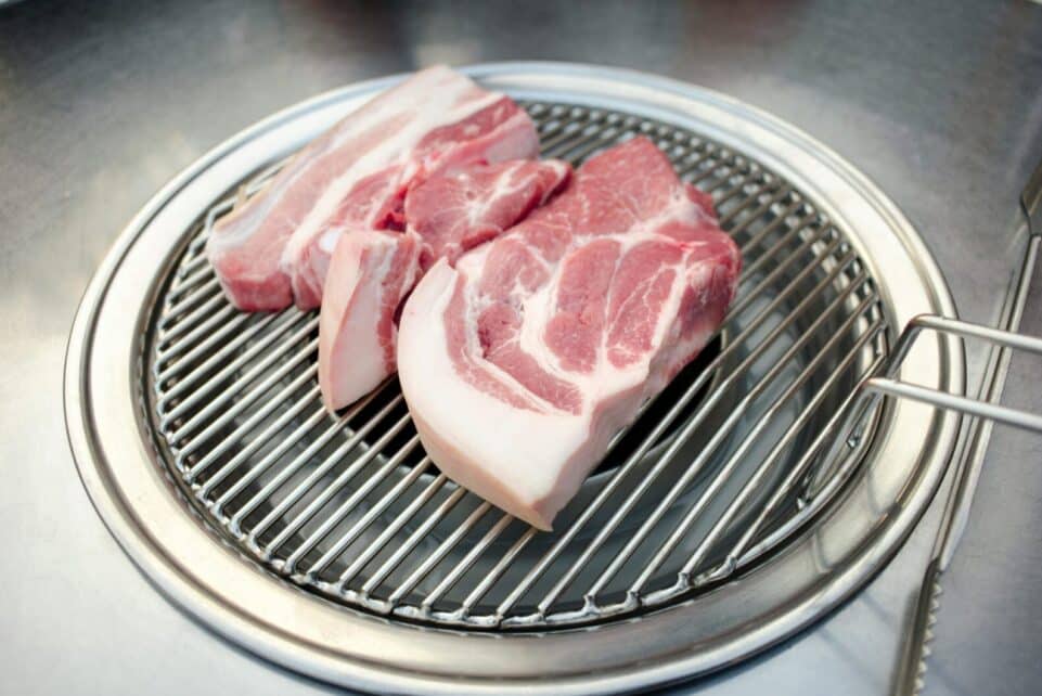 Close-up of raw pork slices on a Korean BBQ grill, ready for cooking.