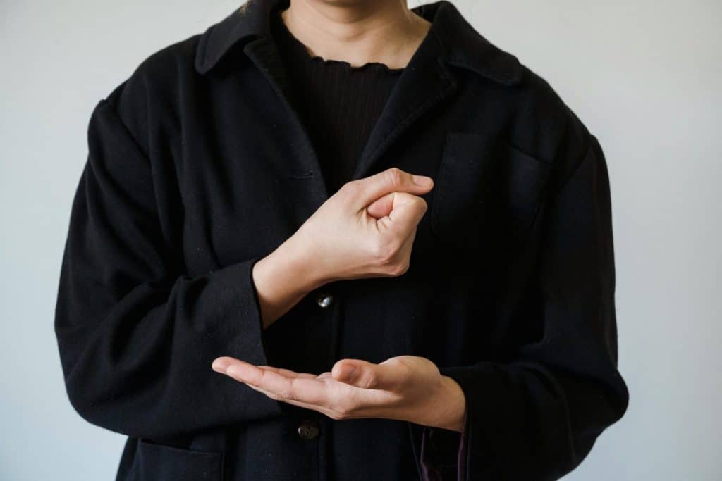 Person demonstrating American Sign Language in a black jacket, focusing on hand gestures.