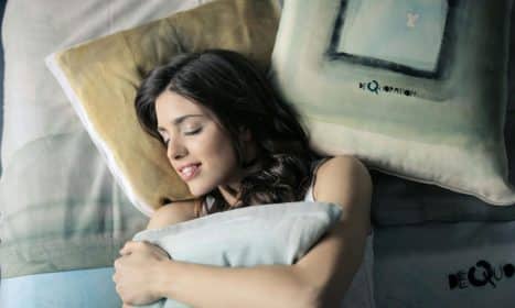 Woman peacefully sleeping in bed, hugging a pillow with a contented smile.