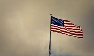 US flag waving in wind against a cloudy sky, symbolizing freedom and patriotism.