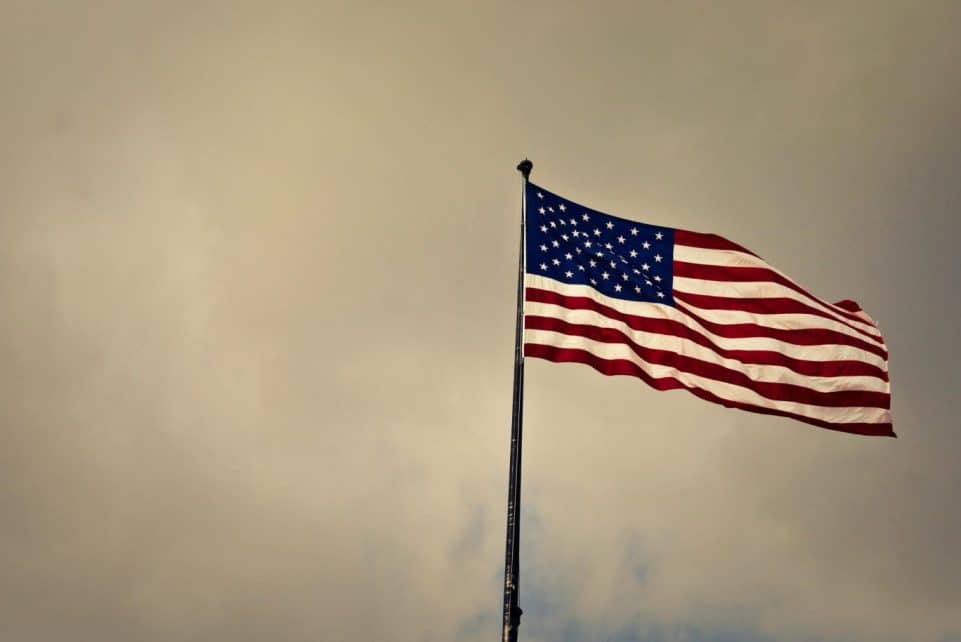 US flag waving in wind against a cloudy sky, symbolizing freedom and patriotism.