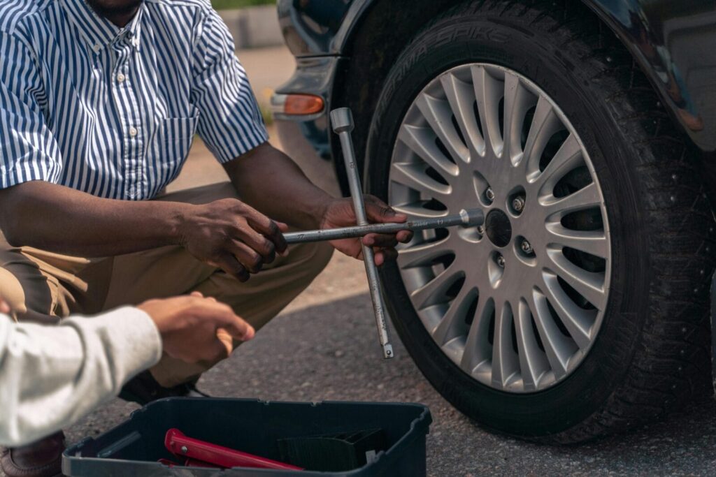 An adult demonstrating how to change a tire to a teenager, focusing on teamwork and learning.