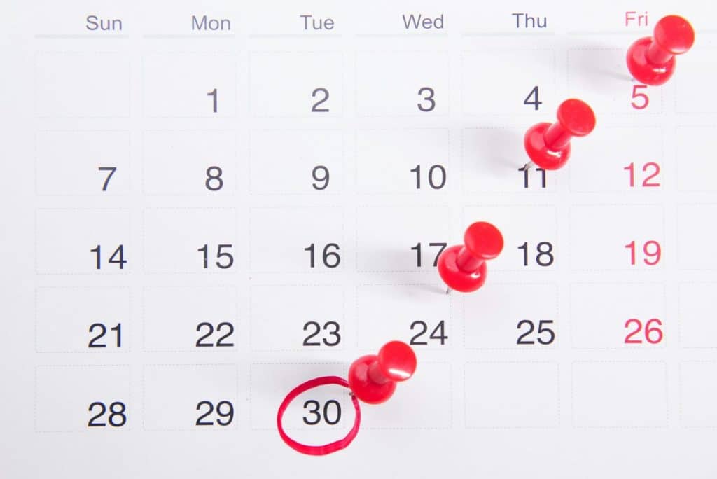 Close-up of a calendar with red push pins marking important dates, emphasizing deadlines.