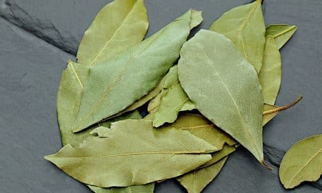 A close-up photo of dried bay leaves on a textured slate surface, ideal for spice and culinary themes.