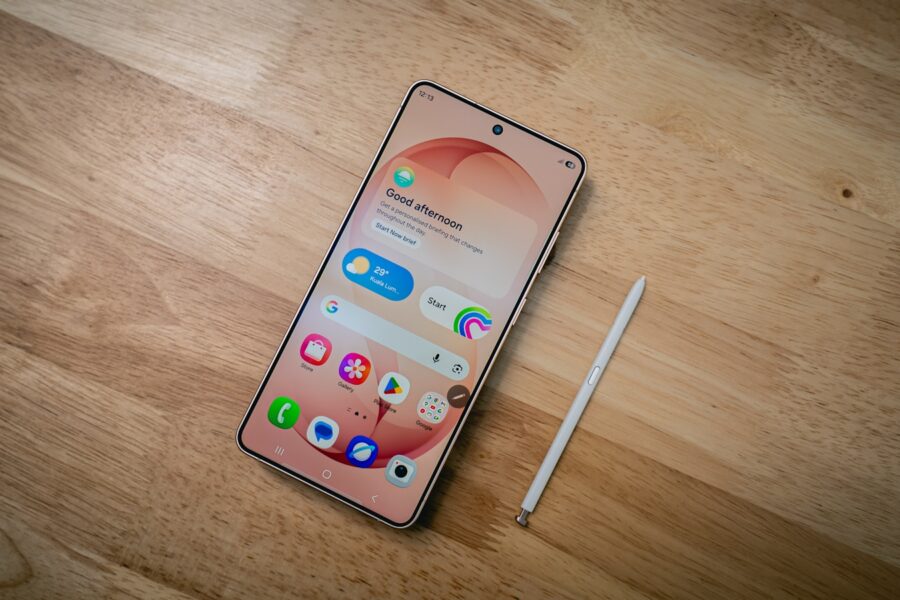 A smartphone with a stylus rests on a wooden surface.