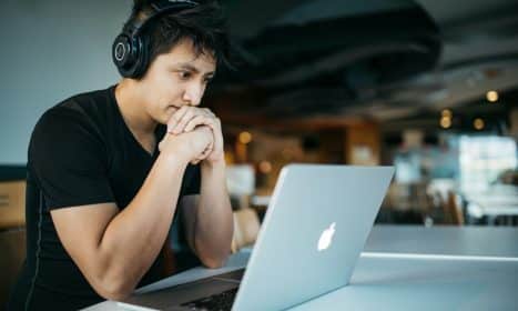 man wearing headphones while sitting on chair in front of MacBook