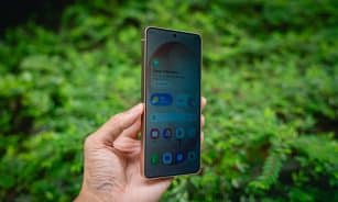 Hand holding a smartphone with green foliage background.