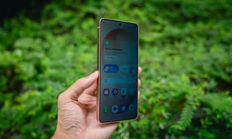 Hand holding a smartphone with green foliage background.