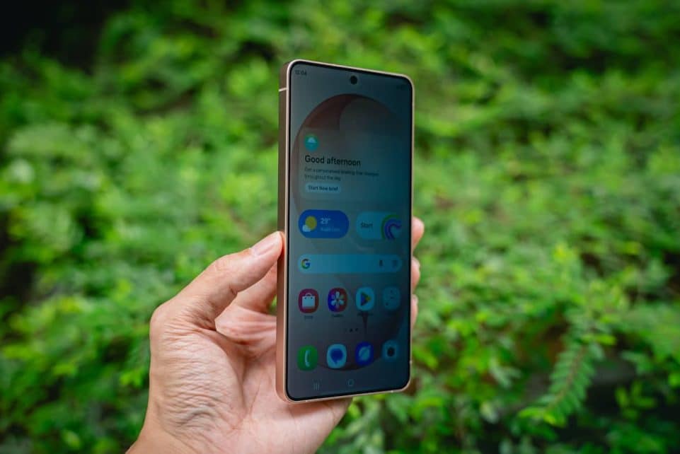 Hand holding a smartphone with green foliage background.